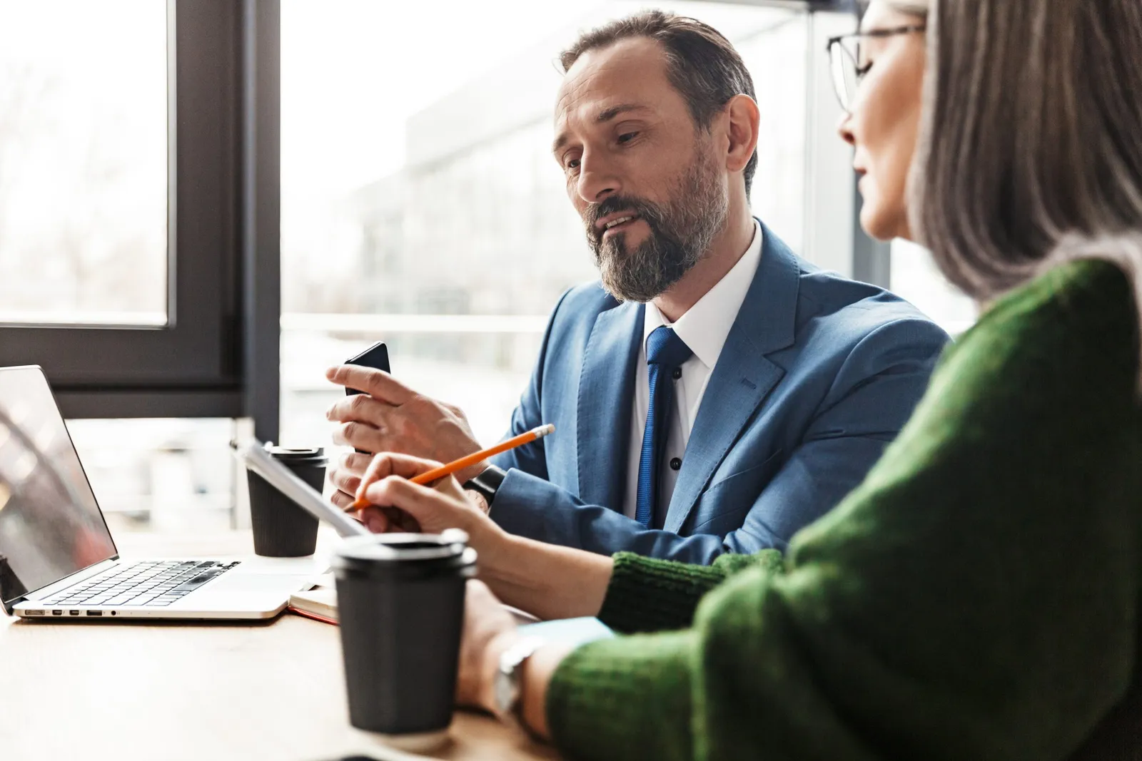 Photo of colleagues talking while working with laptop and documents